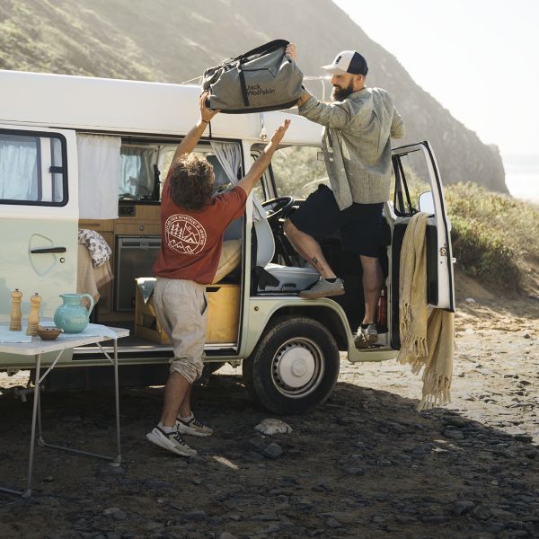 Two men with a travel bag in front of a camper van