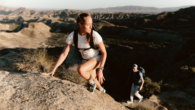 A couple in summery hiking clothes climbing up a rock